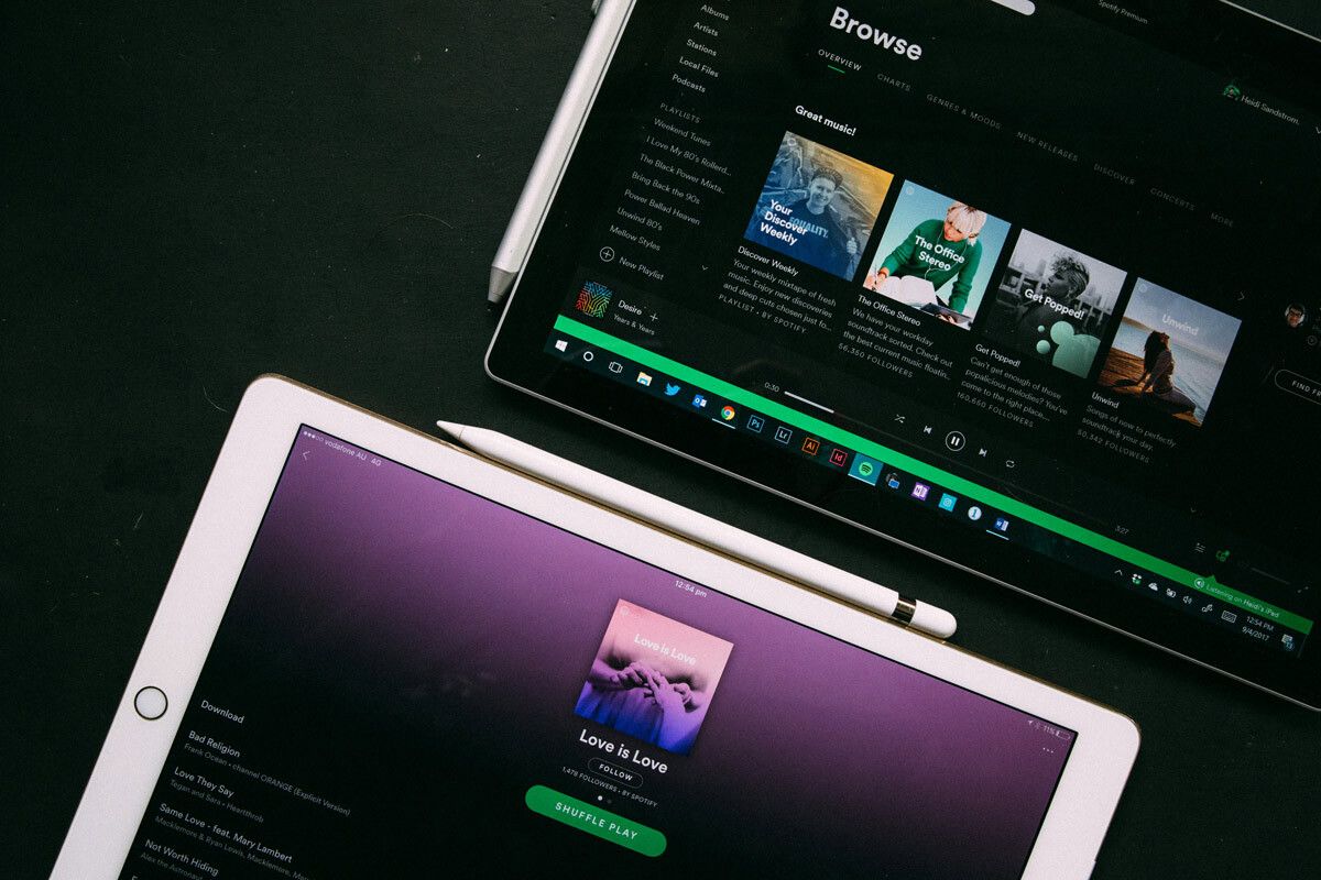 Deux tablettes posées avec leurs stylets sur une table. Une noire et une blanche. Les écrans sont allumés et l'application "Spotify" est ouvert sur les deux écrans.