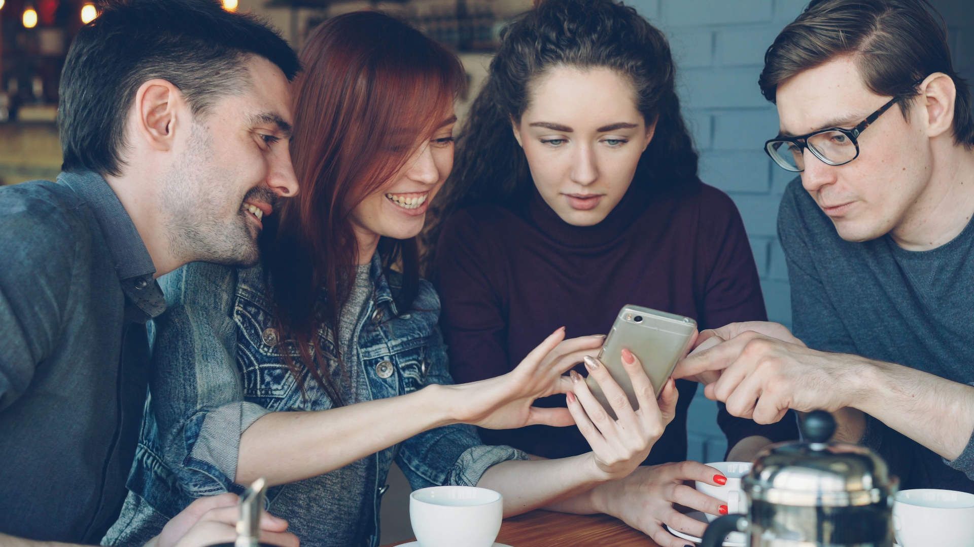 Groupe de 4 personnes regardant un téléphone en souriant